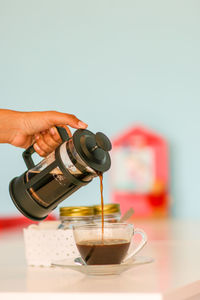 Cropped image of woman pouring coffee in cup from french press coffee maker on table