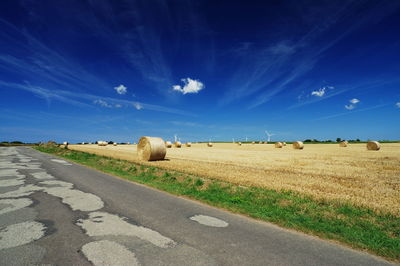 Hay bales on field against blue sky