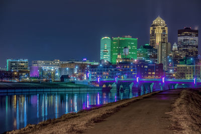 Illuminated buildings by river against sky at night