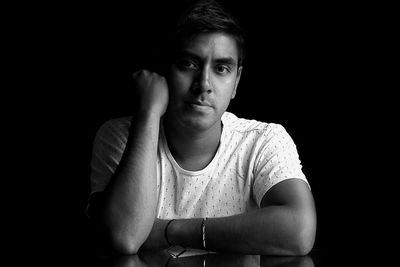 Young man sitting against black background