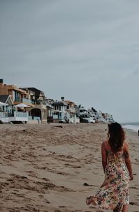 Rear view of woman standing at beach against sky