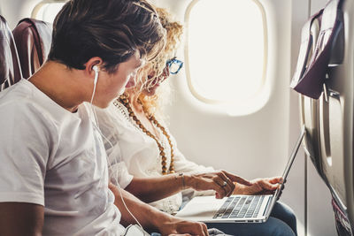 Man and woman using laptop while sitting in airplane