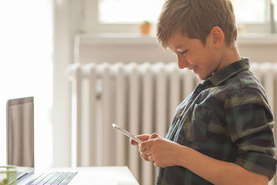 Cute happy boy enjoying while text messaging on mobile phone at home.