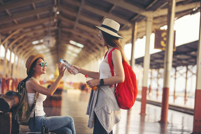 Side view of woman giving water bottle to friend at railroad station