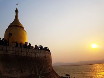 People at temple by sea against sky during sunset