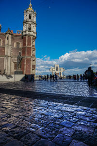 People on street by buildings against blue sky