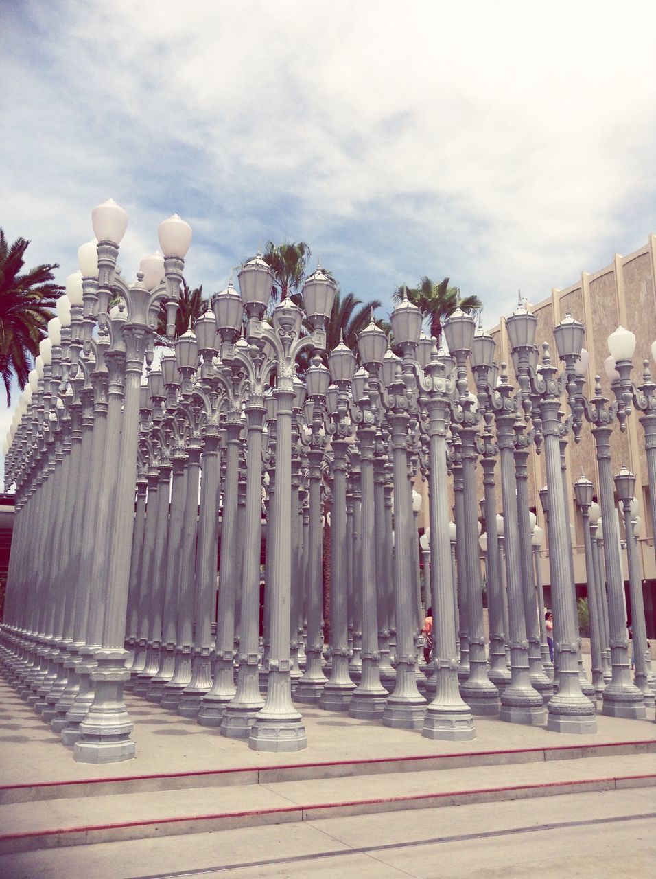 architecture, built structure, building exterior, sky, cloud - sky, in a row, city, cloud, street light, cloudy, railing, day, low angle view, building, outdoors, incidental people, the way forward, flag, architectural column, tree