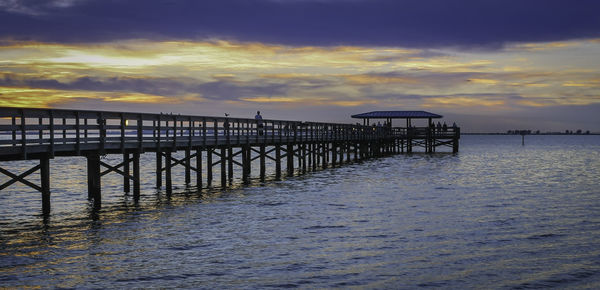 Pier over calm sea against cloudy sky