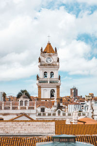 Church amidst buildings against cloudy sky in city