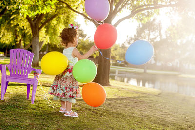 Rear view of girl with balloons against trees