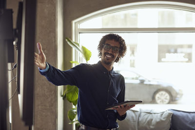 Happy businessman with digital tablet gesturing at creative office