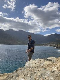 Man standing on rock by mountain against sky
