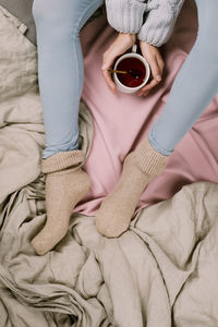 Midsection of woman with coffee cup on bed