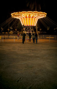 People in illuminated amusement park against sky at night