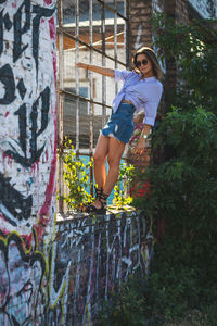 Young woman standing on window sill amidst graffiti wall