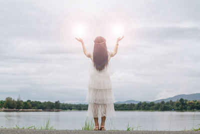 Rear view of woman standing by lake against sky