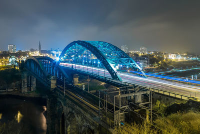 Light trails on bridge in illuminated city at night