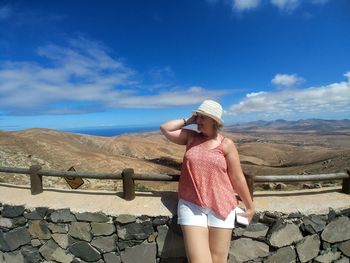 Full length of young woman standing on retaining wall against sky