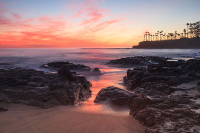 Low angle view of sea and rocks during sunset