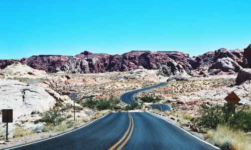 Road leading towards mountains against clear blue sky