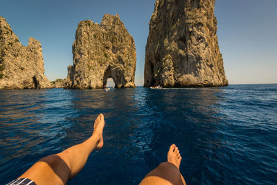 Low section of people on rock by sea against clear sky