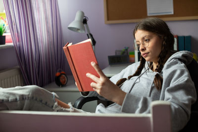 A teenage girl with glasses reads her next school reading with interest.