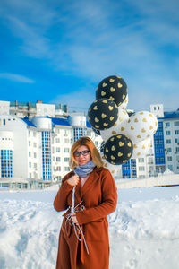 Portrait of woman with balloons standing on snow against sky