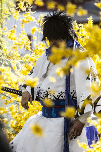 Man wearing samurai costume standing amidst yellow flowers at park