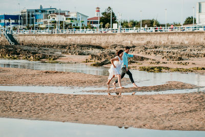 Full length of couple embracing while standing on beach against sky