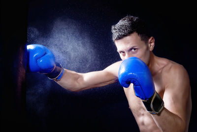 Portrait of young male boxer punching bag against black background