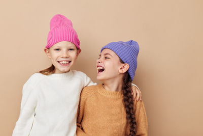 Portrait of smiling sisters wearing knit hat against beige background