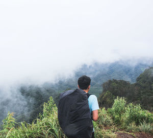 Rear view of backpack man hiking on mountain during foggy weather