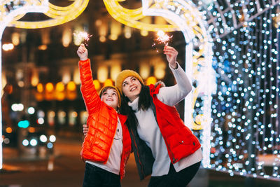 A beautiful boy and his mother celebrate new year or christmas with sparklers on the background 