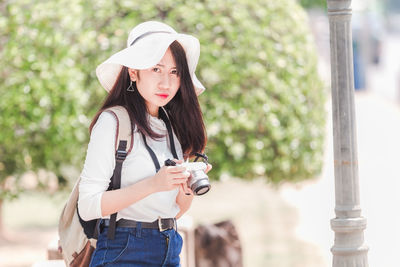 Portrait of young woman holding hat standing outdoors