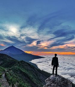 Rear view of man standing on rock against sky during sunset