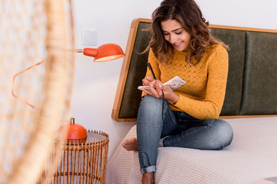 Smiling woman writing in diary while sitting on bed at home