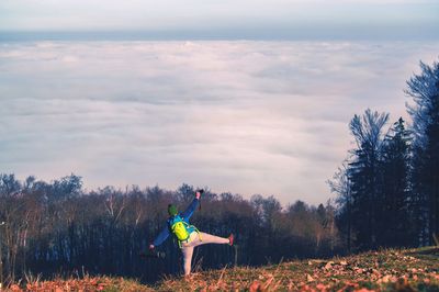 Rear view of boy standing on one leg against cloudy sky