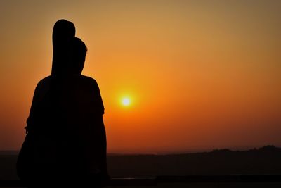 Rear view of silhouette man standing against orange sky