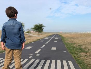 Rear view of boy standing on road against sky