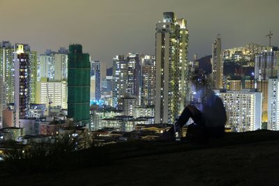 Man with illuminated cityscape against sky at night