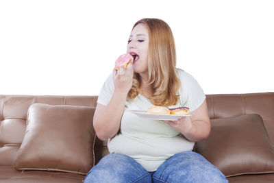 Young woman eating donut while sitting on sofa