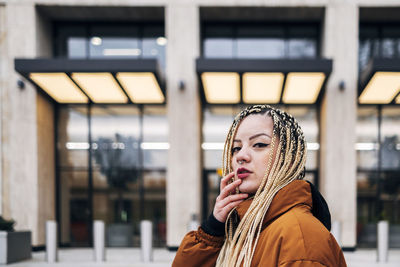 Young woman with hand on chin staring while standing against building