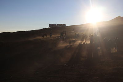 Silhouette people on field against bright sun