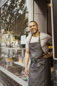 Portrait of smiling male deli owner with hand on hip by doorway