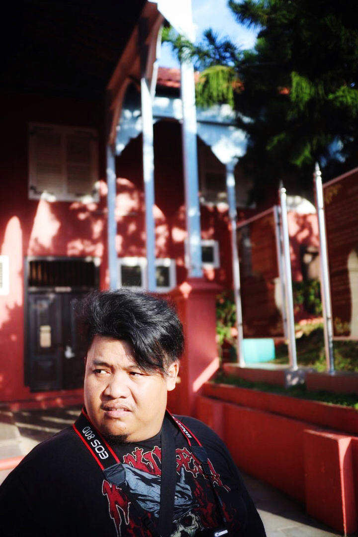 PORTRAIT OF MAN LOOKING AWAY WHILE STANDING AGAINST RED BUILDING