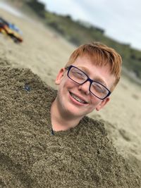 Portrait of smiling teenage boy buried in sand at beach