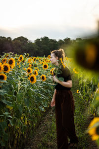 Woman standing by sunflower plants against sky