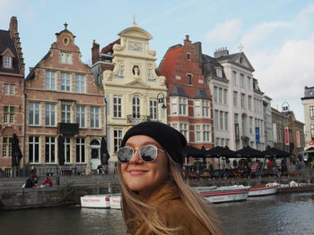 Portrait of young woman in canal against buildings in city