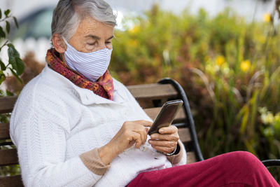 Senior woman wearing mask using smart phone outdoors