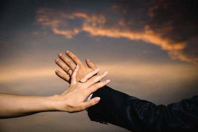Cropped hands of couple wearing wedding rings against sky during sunset